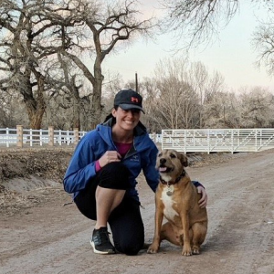Dr. Whitney Jones DVM kneeling next to her dog on a dirt path, highlighting the bond between pets and their owners.