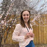 Cassidy Stone, smiles outdoors with blossoming trees in the background, symbolizing her friendly and approachable nature.